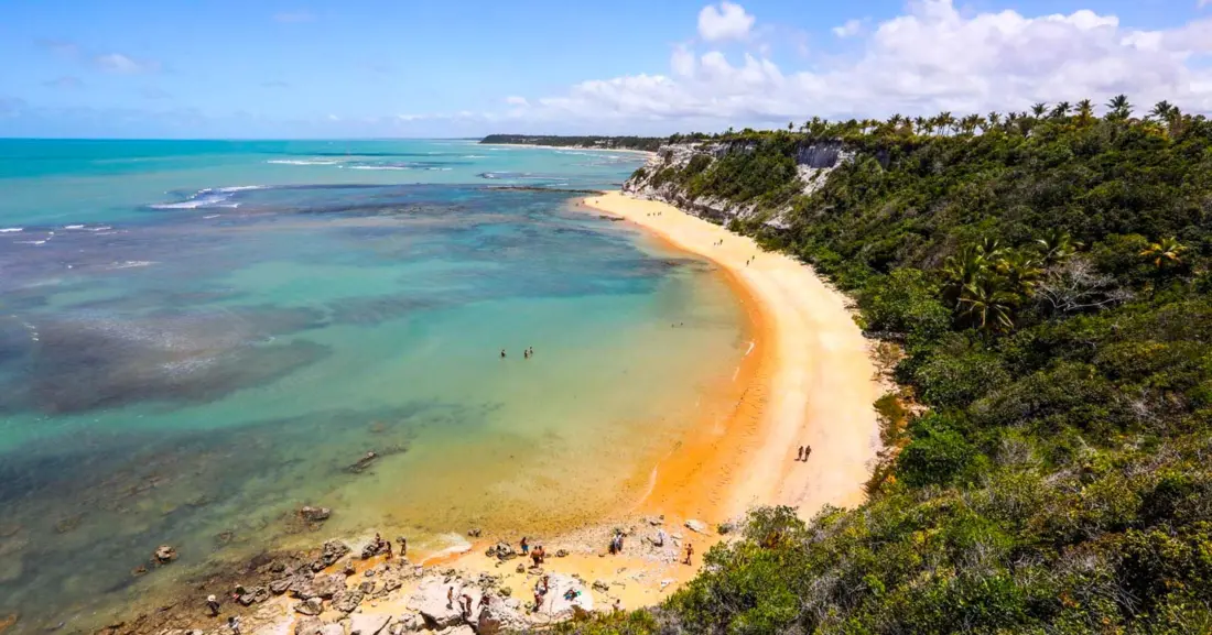 Praia cercada por falésias e vegetação no sul da Bahia